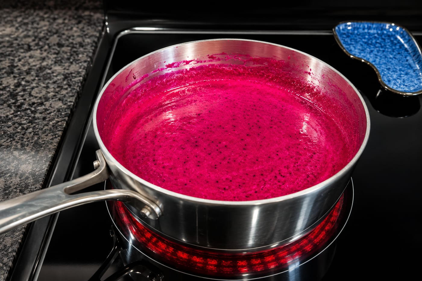 Dragon fruit jam simmering in a stainless saucepan, its color a brilliant magenta flecked with black seeds.